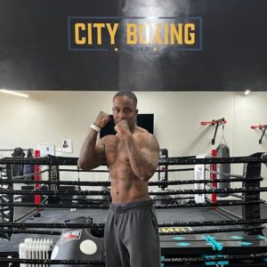 Personal trainer, holding fists up in Boxing gym, infront of ring